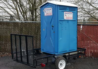 Blue portable restroom secured to a black utility trailer with a ramp, designed for easy mobility and rapid deployment in the field.