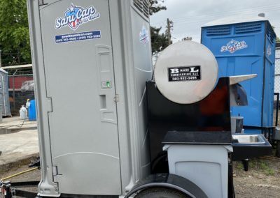 A mobile, trailer-mounted portable toilet unit featuring an integrated exterior sink for industrial or remote job site sanitation.